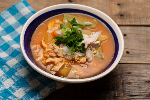 Traditional mexican chicken soup with vegetables and rice on wooden background