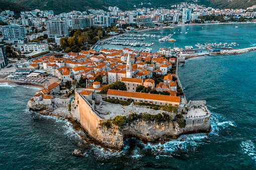 Drone point of view at the old town Budva surrounded by the big wall and the city of Budva with its new buildings and marina in fron of it..