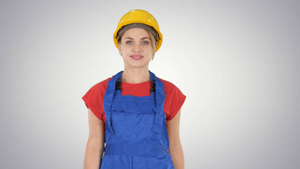 istock Young woman in yellow hardhat walking on gradient background 1276513464
