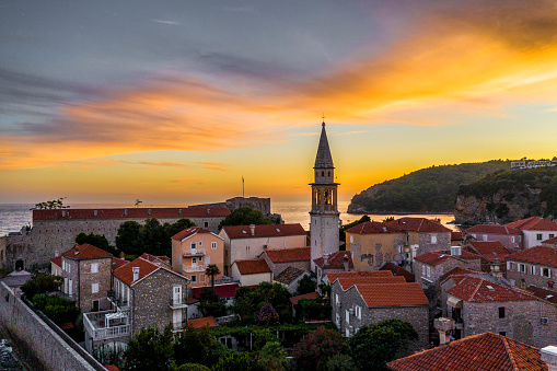 Spectacular scenery captured with a drone and showing church tower in the old town Budva surrounded by old houses  and illuminated by the sunset light.