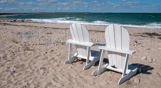 Two wooden Adirondack chairs rest on rocky Town Neck Beach in Sandwich, Massachusetts near the entrance of the Cape Cod Canal.