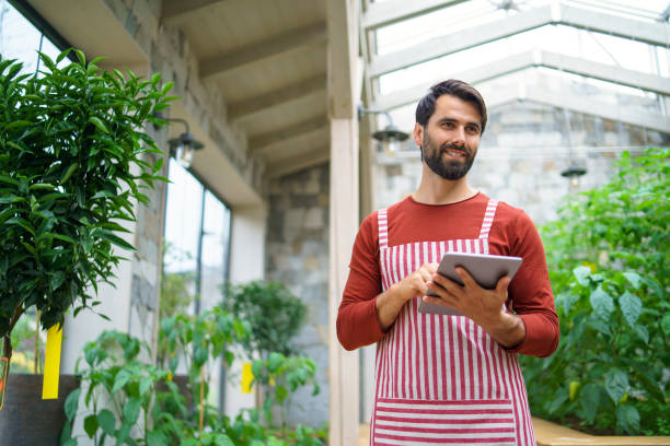 istock Man gardener with tablet standing in greenhouse, working. 1276517151