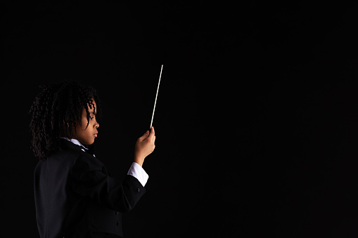 African-American girl in tuxedo conducting with baton against a black background