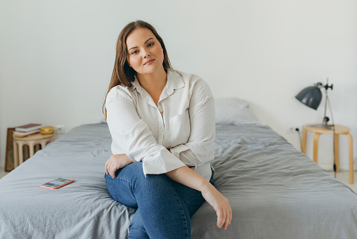 Retrato de una mujer segura más tamaño sentada en su cama, mirando a la cámara photo
