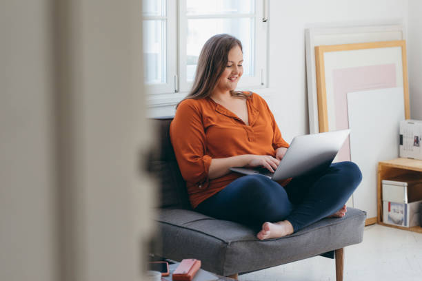 istock Happy Plus Size Woman Wearing Orange Using her Laptop Computer to Work from Home 1276522897