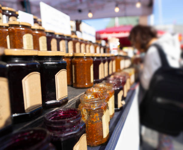 Person tasting jam or marmalade from glass jars at outdoor farmers market