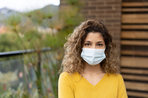 Portrait of a young Latin American woman wearing a facemask outdoors in the terrace of her house during the COVID-19 pandemic