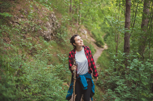 View of a young woman in her outdoor pursuit. She's adventurously overcoming the most difficult parts of the route with a help of a stick, while enjoying beauties of nature all around her.