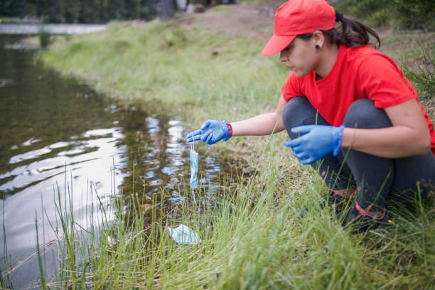 istock Young Ecology Responsible Woman Is Taking A leftover Protective face Mask From The Lake 1276533596