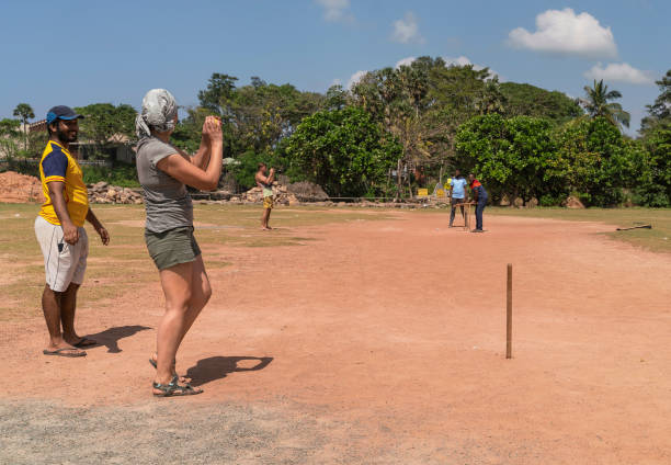 50-jährige kaukasische weiße frau, die touristin, lernt, wie man cricket zusammen mit dem lokalen straßenteam in sri lanka spielt. sie schleudert den ball, spielt krugrolle. - 30s women asian ethnicity 35 40 years stock-fotos und bilder