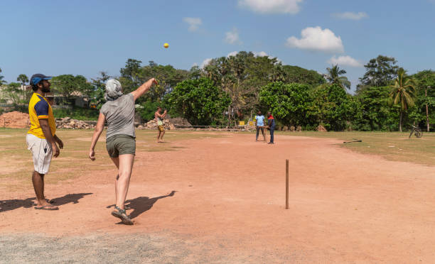 50-jährige kaukasische weiße frau, die touristin, lernt, wie man cricket zusammen mit dem lokalen straßenteam in sri lanka spielt. sie schleudert den ball, spielt krugrolle. - 30s women asian ethnicity 35 40 years stock-fotos und bilder