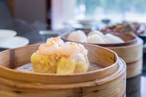 traditional chinese Hong Kong dim sum steamed fresh hot siew mai meat dumpling in bamboo basket on grey wood table background breakfast halal food menu for restaurant asian cafe