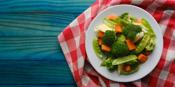 istock Fresh steamed broccoli, cabbage, carrots, sweet peas and cauliflower on a white ceramic plate on a red and white chequered red gingham tablecloth set on a vibrant blue/turquoise wood grained table background. 1276544382
