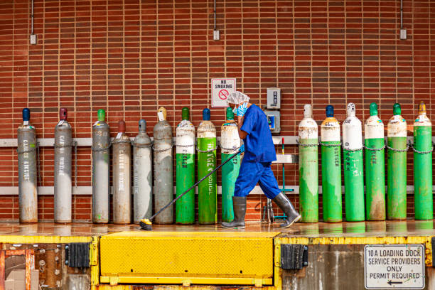 un conserje está limpiando el muelle de carga de un hospital con enormes tanques de oxígeno y carbondióxido en segundo plano - scrub brush fotografías e imágenes de stock