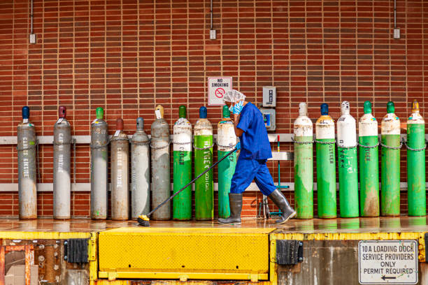 un concierge nettoie le quai de chargement d’un hôpital avec d’énormes réservoirs d’oxygène et de carbondioxide à l’arrière-plan - scrub brush photos et images de collection