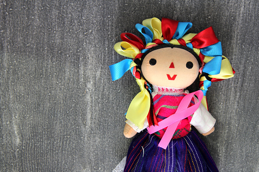the Mexican handmade doll with pink ribbon on vintage gray wooden background for campaign against breast cancer