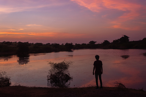 Silhouette of an Indian man standing in front of the lake during the sunset
