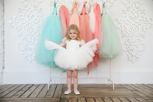 fancy dresses for girls. baby in a white, lush, elegant dress near the hanger with festive clothes. fashion for children. shop.