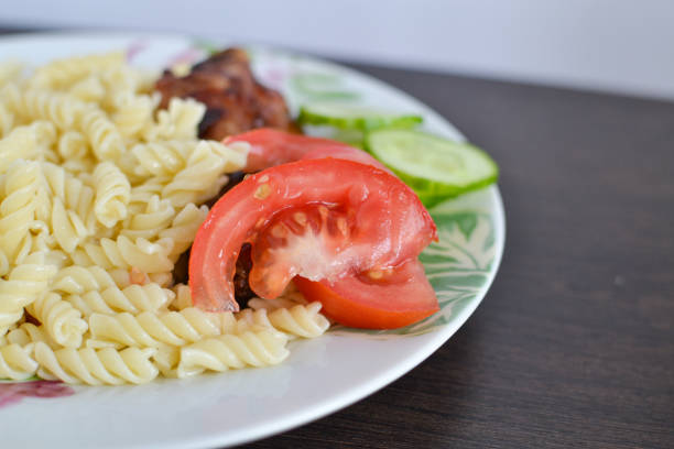 Healthy dinner with pasta, chicken and vegetables close-up. Chopped fresh green cucumbers and red tomatoes. Spiral pasta with vegetables. A hearty and simple lunch.
