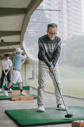 Asian chinese active senior man golfer teeing off and swing his diver  golf club at golf driving range