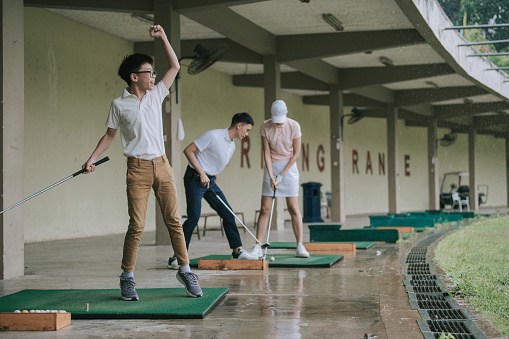 Asian chinese young boy practicing golf in driving range with his parents during raining