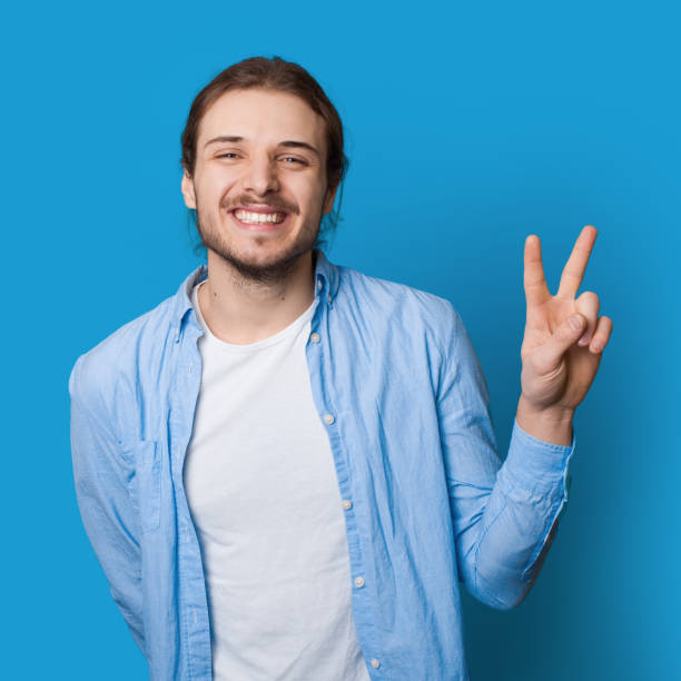 istock Toothily smiling man with beard and long hair gesturing peace and friendship on a blue studio wall 1276564793