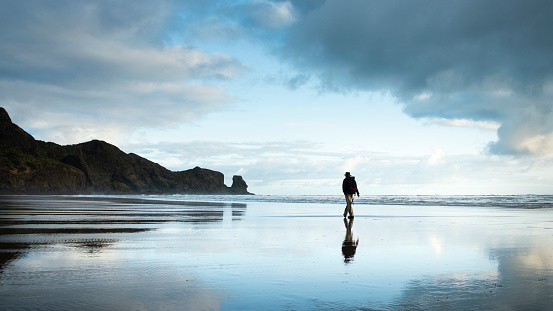 An active senior woman of Hawaiian and Chinese descent who is wearing a winter jacket, takes a relaxing walk along an empty beach in Bandon, Oregon with beautiful rock formations while on a winter trip.