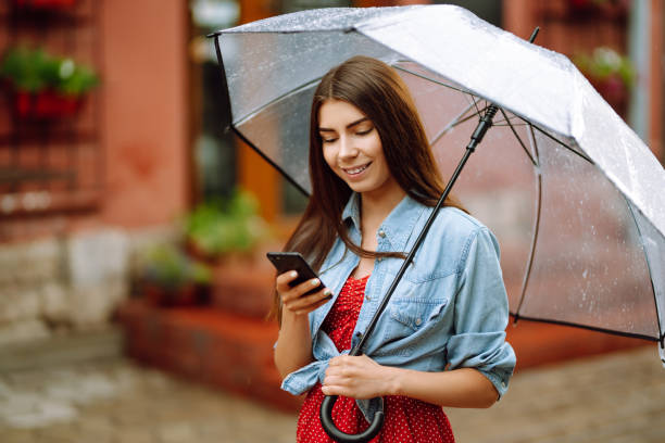 istock Cheerful woman holding umbrella and using phone while strolling outside. 1276571582