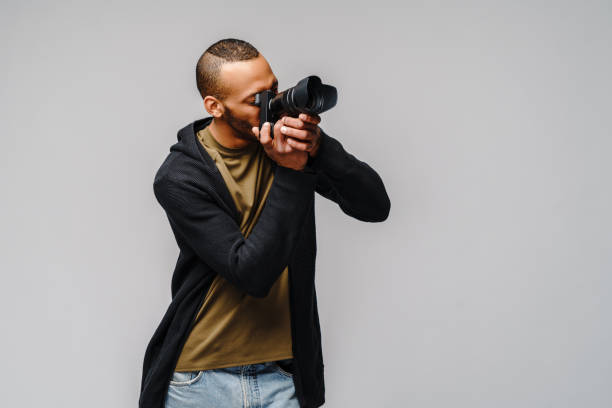 istock Handsome african american guy holding digital camera over light gray background 1276574217