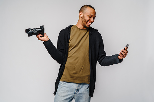 Handsome african american guy holding digital camera over light gray background.