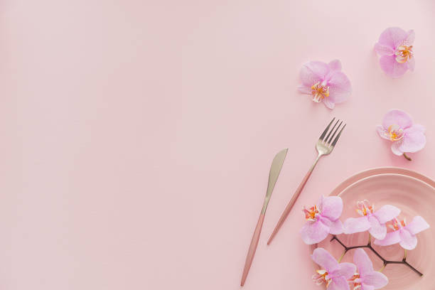 istock Flower and table settings overhead composition on light pink background. Pink ceramic plates, cutlery and perple orchid flowers. Holiday modern table decoration. Romantic date. 1276575109