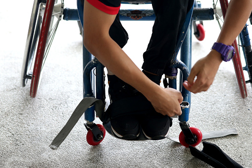 A wheelchair-bound Muslim young man is strapping his legs on wheelchair.