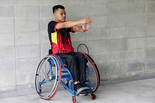 A wheelchair-bound Muslim young man is doing light exercise before gearing ready to enjoy badminton game.