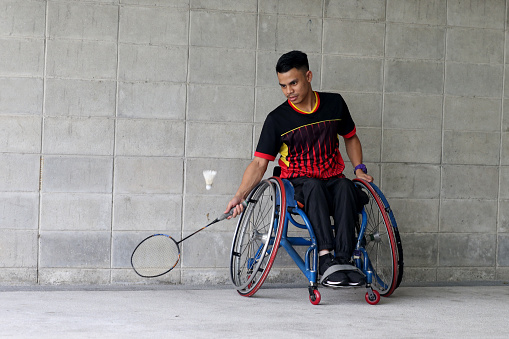 A wheelchair-bound Muslim young man is enjoying playing badminton.