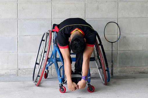 A wheelchair-bound Muslim young man is doing light exercise before gearing ready to enjoy badminton game.
