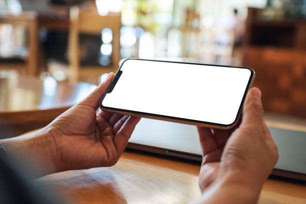 istock a woman holding mobile phone with blank white desktop screen with laptop on the table 1276580193