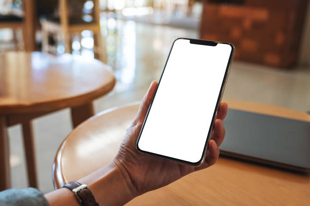 istock a woman holding mobile phone with blank white desktop screen with laptop on the table 1276580218