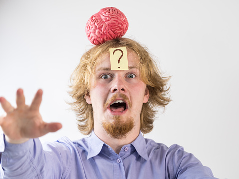 Young guy playing with human brain model. Man discovering innovation and thinking having question mark on his head.