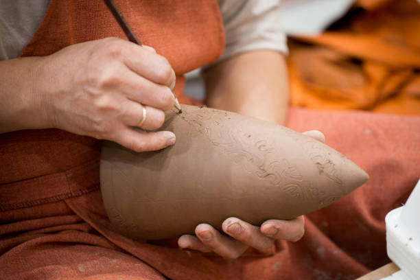 istock Ceramic workshop, the master puts otnament on unfired earthenware jug. Close-up of master hands. Made by hand, a hobby. Background illustrating the manual work with clay. 1276584420