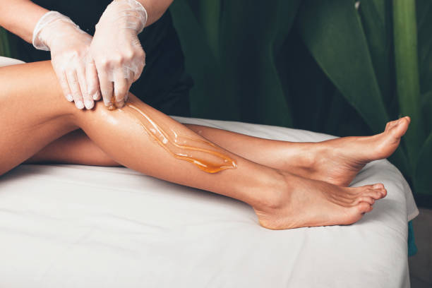 procedimiento de depilación del cabello de las piernas realizado en el moderno salón de bienestar por una mujer que usa guantes - wax fotografías e imágenes de stock