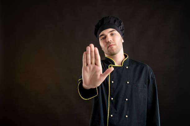 istock Young male dressed in a black chef suit showing stop sign 1276587625