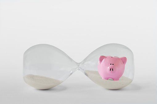 Hourglass with piggy bank lying on white background - Concept of economy savings and stopping time