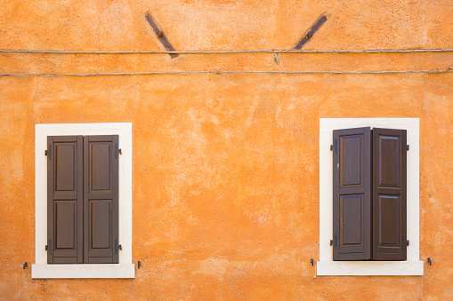 Old orange house facade, closed brown window shutters in popular touristic historic village Garda, Italy