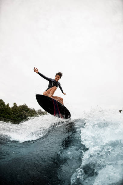 istock cheerful woman in black wetsuit effectively jumps on surfboard on wave 1276594136