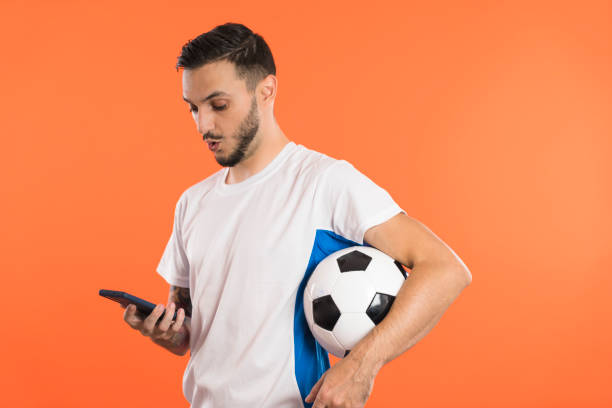 joueur de football excité ou ventilateur avec la boule sous le bras regardant son smartphone étonné. concept de publicité - fan hooligan screaming shouting photos et images de collection