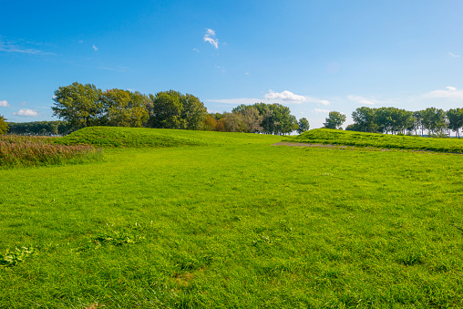 Dike in a green grassy field in sunlight under a blue sky in autumn, Almere, Flevoland, The Netherlands, September 24, 2020