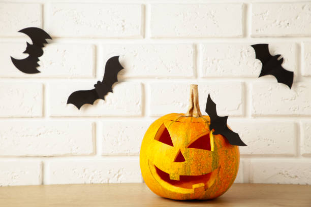 istock Carved glowing pumpkin and black bats on light background. Halloween celebration 1276604463