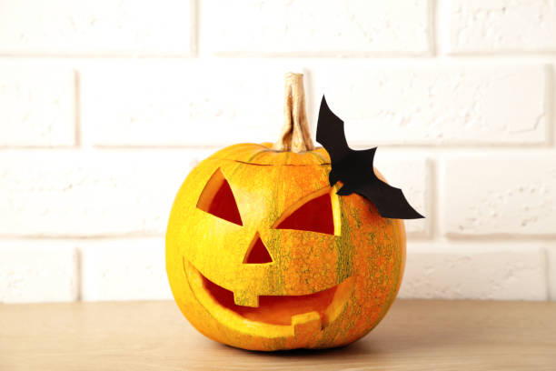 istock Carved glowing pumpkin and black bat on light background. Halloween celebration 1276604807