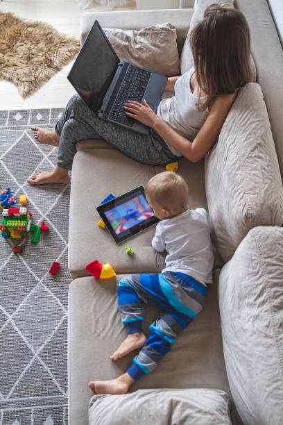 istock mom works at home sitting on couch with laptop while her little 1276605546