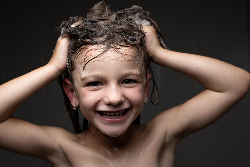 Closeup portrait of a happy smiling little girl in the shower with soap foam in the hair. Child health care and hygiene at bath time concept.